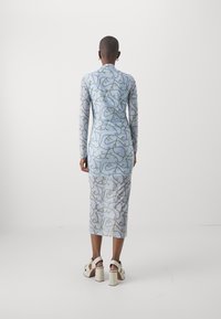 Abito attillato a maniche lunghe di colore azzurro chiaro con un motivo a spirale e dettagli dorati, abbinato a sandali piattaforma bianchi con accessori in oro.