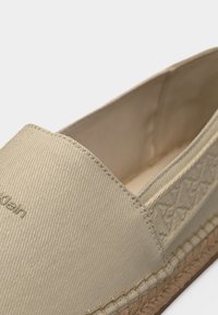 Κοντινό πλάνο σε μπεζ παντόφλα espadrille με υφασμάτινο επάνω μέρος με υφή και λεπτομέρεια πλεγμένης σόλας από ζούτα.