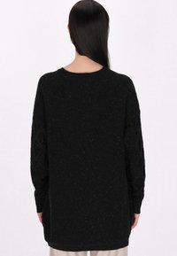 Schwarzer Strickpullover mit langen Ärmeln, gerundetem Halsausschnitt und strukturiertem Muster. Weiches Material mit dezentem Schimmer und lockerer Passform.