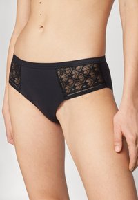 Zwarte bikini slips met kant aan de zijkanten in een geometrisch patroon, een gladde textuur en een elastische tailleband voor comfort.