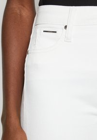 Jeans de denim blanco con un diseño clásico de cinco bolsillos, acentos de hardware plateado y una textura suave. Cuenta con una etiqueta metálica de marca en el bolsillo.