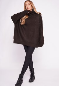 Übergroßer dunkelbrauner Strickpullover mit hohem Rollkragen, kombiniert mit schwarzen Leggings und schwarzen Combat Boots. Glatte Textur, lässige Passform.