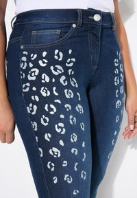 Jeans dżinsowe w ciemnoniebieskim kolorze z jasnoszarym wzorem w panterkę po bokach. Posiadają klasyczny pięciokieszeniowy design i zapięcie na guzik.