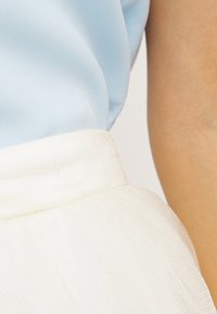 Blusa de satén azul claro con una falda blanca texturizada que presenta una cinturilla amplia y suave. La tela muestra un brillo sutil y una caída suave.