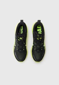 Baskets de course noires avec une tige en mesh, présentant des accents vert fluo, une semelle épaisse et un système de laçage traditionnel. Logo visible sur le côté.
