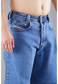 Blaue Denim-Jeans mit geradem Bein, Kupferrivets und einer kleinen Vordertasche. Das Material zeigt eine klassische Twill-Struktur.