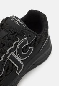Zapatilla negra con material de malla, suela de goma y acentos prominentes de logo blanco. Punta redondeada y cuello acolchado para mayor comodidad.