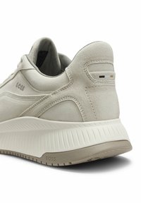 Talons de baskets BOSS en daim beige avec semelle intermédiaire blanche texturée, semelle extérieure grise et petits détails de logo noirs, blancs et beige à l'arrière.