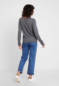 Maglione grigio a maniche lunghe con scollatura tonda, abbinato a jeans blu a gamba dritta e sneakers bianche con dettagli in stampa leopardata.
