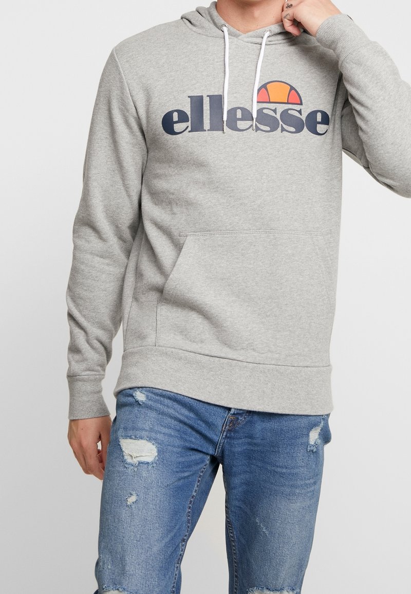 Sudadera gris con capucha y cordones blancos, presenta un gran logo "ellesse" en navy y naranja, bolsillo canguro frontal, puños y dobladillo acanalados.