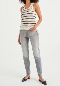 Stickad linne i krämfärg med ett vågigt brunt mönster, kombinerat med ljusgrå slim-fit-jeans och svarta spetsiga ballerina-skor.