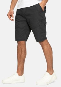 Shorts cargo de color gris oscuro hechos de una mezcla de algodón, con bolsillos laterales, cierre de botón y un ajuste relajado. Se llevan con zapatillas blancas.