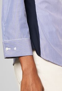 Randig skjorta i blått och vitt med en knäppt manschett, som har en len tygkänsla och en sidoklyvning vid fållen.