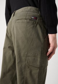 Olivově zelené cargo kalhoty s texturovaným povrchem, které mají zadní kapsu, boční kapsu a nášivku s logem Tommy Jeans.