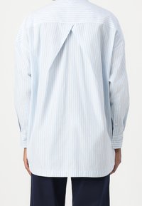 Ljusblå och vit vertikalt randig långärmad skjorta med en central inverterad veck på baksidan, kombinerad med mörkblå byxor.