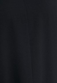 Close-up of black fabric with a vertical seam running down the center, showing texture and stitching details.