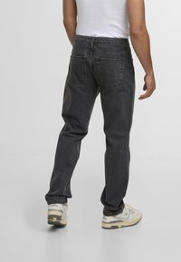 Mørk grå denimjeans med rett ben, med baklommer og en falmet vask. Brukt sammen med lysfargede joggesko.