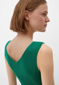 Robe en tricot vert à côtes avec un dos en V et de larges bretelles. Met en valeur la texture et le design ajusté vue de profil.