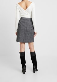 Haut blanc à manches longues avec un dos en V, associé à une mini-jupe en chevrons gris. Le mannequin porte des bottes noires montantes avec un talon carré.