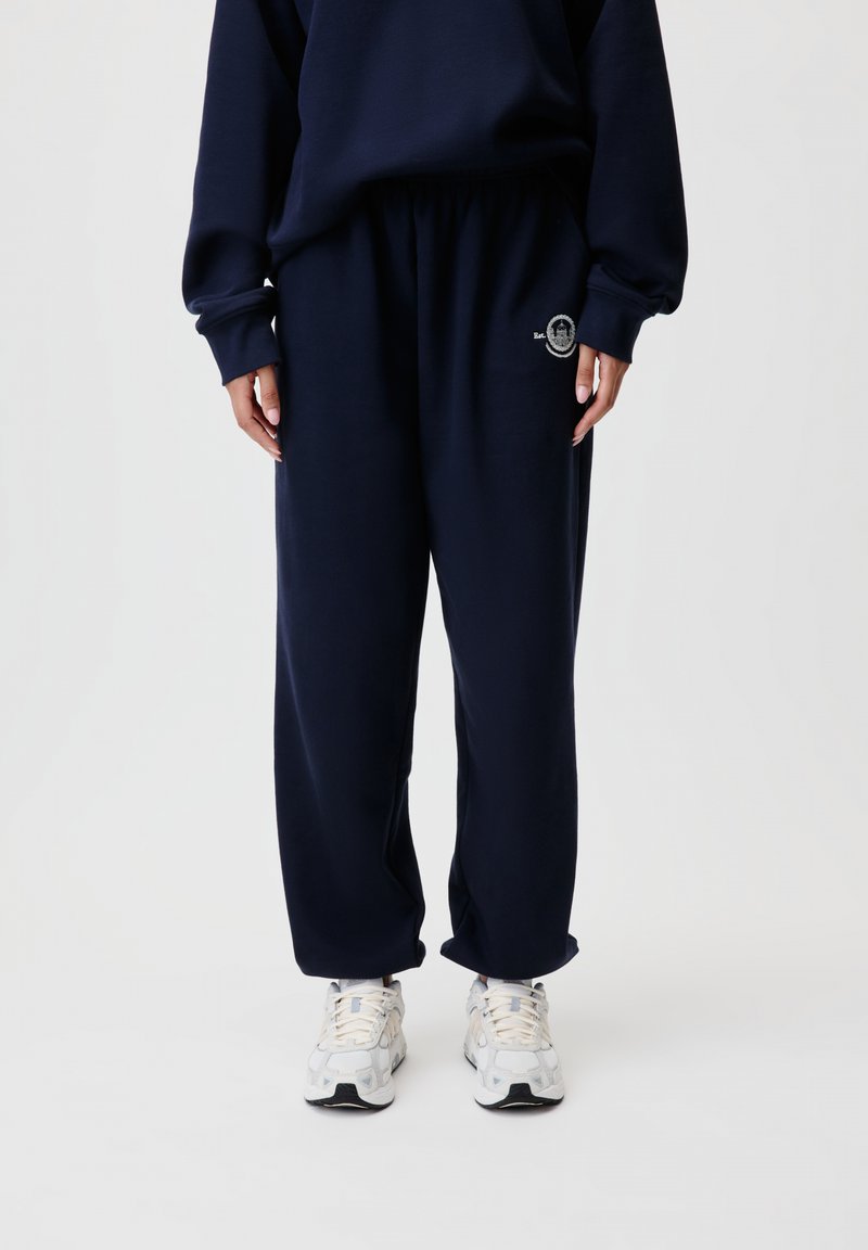 Navyblaue Sweatpants aus weichem Stoff mit einem elastischen Bund, versehen mit einem kleinen bestickten Logo auf der linken Seite.