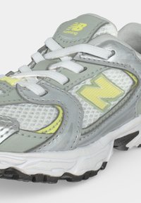 Γκρι και άσπρο παπούτσι για τρέξιμο New Balance με κίτρινες λεπτομέρειες και λευκά κορδόνια σε κοντινό πλάνο.