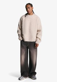 Beiger flauschiger Pullover mit gerippten Bündchen, kombiniert mit weit geschnittenen dunklen Jeans mit leichter Ausbleichung und grauen Sportschuhen.