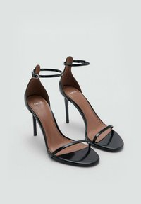 Sandale cu toc înalt din piele patent neagră, cu o curea subțire la gleznă și design cu vârf pătrat. Tălpică interioară maro cu logo-ul brandului.