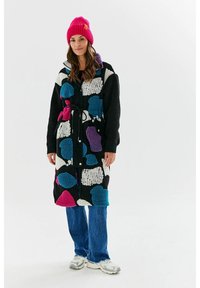 Czarny płaszcz polarowy z kolorowymi abstrakcyjnymi wzorami w odcieniach fioletu, niebieskiego i białego. Posiada pasek, guziki i kieszenie; zestawiony z niebieskimi dżinsami.