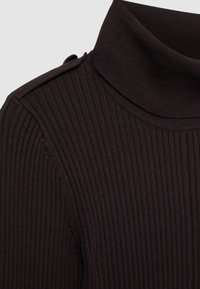Mörk randig polotröja med hög krage och knappdetalj på axeln. Texturen är mjuk och sträcker sig.