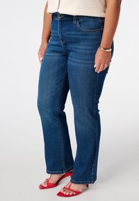 Blauwe denim jeans met een rechte pasvorm, voorzien van gestikte details en een middelhoge tailleband. Gecombineerd met rode strappy sandalen.