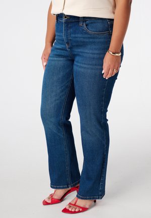 Blauwe denim jeans met een rechte pasvorm, voorzien van gestikte details en een middelhoge tailleband. Gecombineerd met rode strappy sandalen.