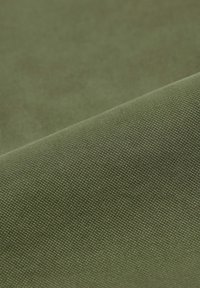 Tessuto in tela khaki, superficie strutturata con un sottile motivo a trama, piegato per mostrare profondità e dimensione. Finitura liscia, colore tenue.