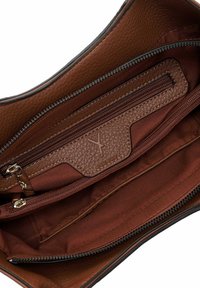 Intérieur d'un sac à main en cuir marron avec plusieurs compartiments zippés et doublure en tissu, présentant des détails de logo en relief sur le rabat de la poche.