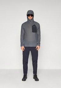 Gray long-sleeve top with hood and a black pocket, paired with dark navy pants. The outfit features a textured fabric and athletic design.
