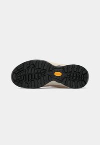 Sola de sapato de exterior bege com sola de borracha Vibram preta, apresentando ranhuras profundas para tração em vários tipos de terreno.