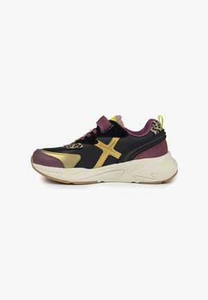 Sneaker nera con accenti dorati, tallone e collo viola, dettaglio in stampa leopardo, materiali testurizzati e suola bianca spessa.