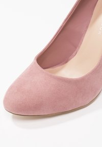 Růžové semišové lodičky s kulatou špičkou, hladkým vnitřkem a mírným podpatkem. Design má čistou siluetu a žádné další ozdoby.