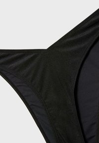 Bas de bikini noir pour femme avec tissu lisse et couture contour sur un fond gris clair uni.