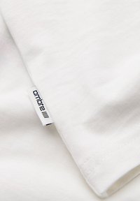 Tissu en coton blanc avec une petite étiquette blanche portant l'inscription « ombre » cousue dans la couture, montrant la texture du tissu et les détails de la couture.