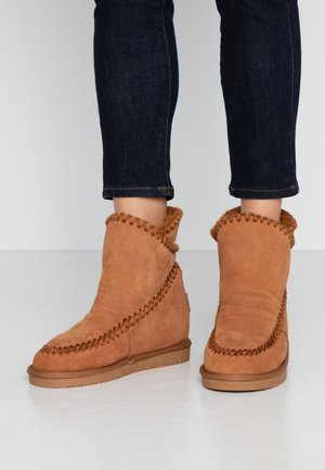Bottes ankle en suède beige avec un revers replié, des coutures décoratives le long de la couture et une semelle en caoutchouc, associées à un jean en denim foncé.