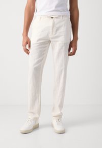 Vita linnebyxor med avslappnad passform, med knappstängning framtill och bältesöglor. Kombinerade med vita sneakers för en avslappnad look.