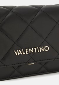Portafoglio in pelle nera trapuntata con logo dorato "Valentino" e cuciture accentuate. La superficie è liscia con motivi a forma di diamante.