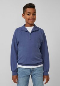 Fleece pullover in diepblauw, met een kwart rits, raglanmouwen en geribbelde manchetten, laag over een wit shirt. Lichte denim jeans.