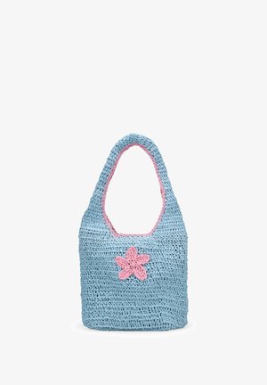 Bolso de ganchillo azul con una decoración de flor rosa y ribete rosa alrededor del asa y la abertura, de pie sobre un fondo blanco.