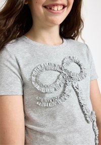 Grå bomulds t-shirt med et dekorativt rynket design formet som en sløjfe på fronten. Korte ærmer og rund halsudskæring.