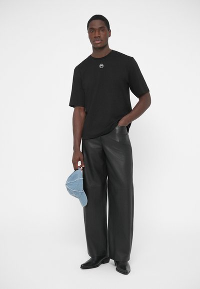 Juoda trumpomis rankovėmis marškinėliai su apskritu logotipu, derinami su plačiomis juodomis odinėmis kelnėmis. Laiko mėlyną džinsinę kepurę. Visas drabužis pasižymi lygiu audiniu.