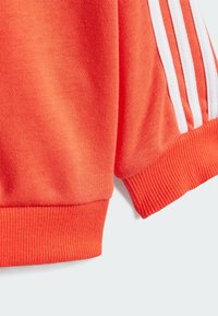 Felpa arancione con strisce bianche, polsini e orlo a costine, morbido al tatto e dal design rilassato, che mette in risalto elementi di stile atletico.