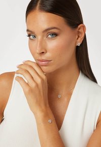 Srebrny zestaw biżuterii zawierający kolczyki w kształcie serca, naszyjnik i bransoletkę. Delikatne łańcuszki z małymi, błyszczącymi akcentami. Gładka powierzchnia.