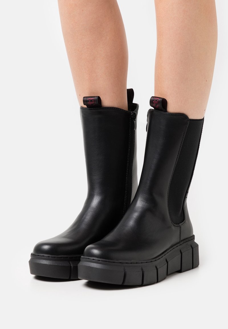 Botas de tobillo de cuero negro con suela de plataforma gruesa, que cuentan con paneles elásticos laterales y una cremallera para facilitar su uso.