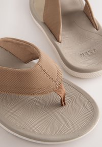 Braune Flip-Flops aus strukturiertem Gummi mit einem gestreiften Stoffriemen. Gepolsterte Innensohle mit Wellenmustern und weiße Gummiaußensohle.